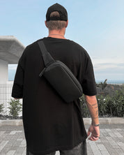 Person wearing a black t-shirt and carrying a black crossbody bag outdoors.