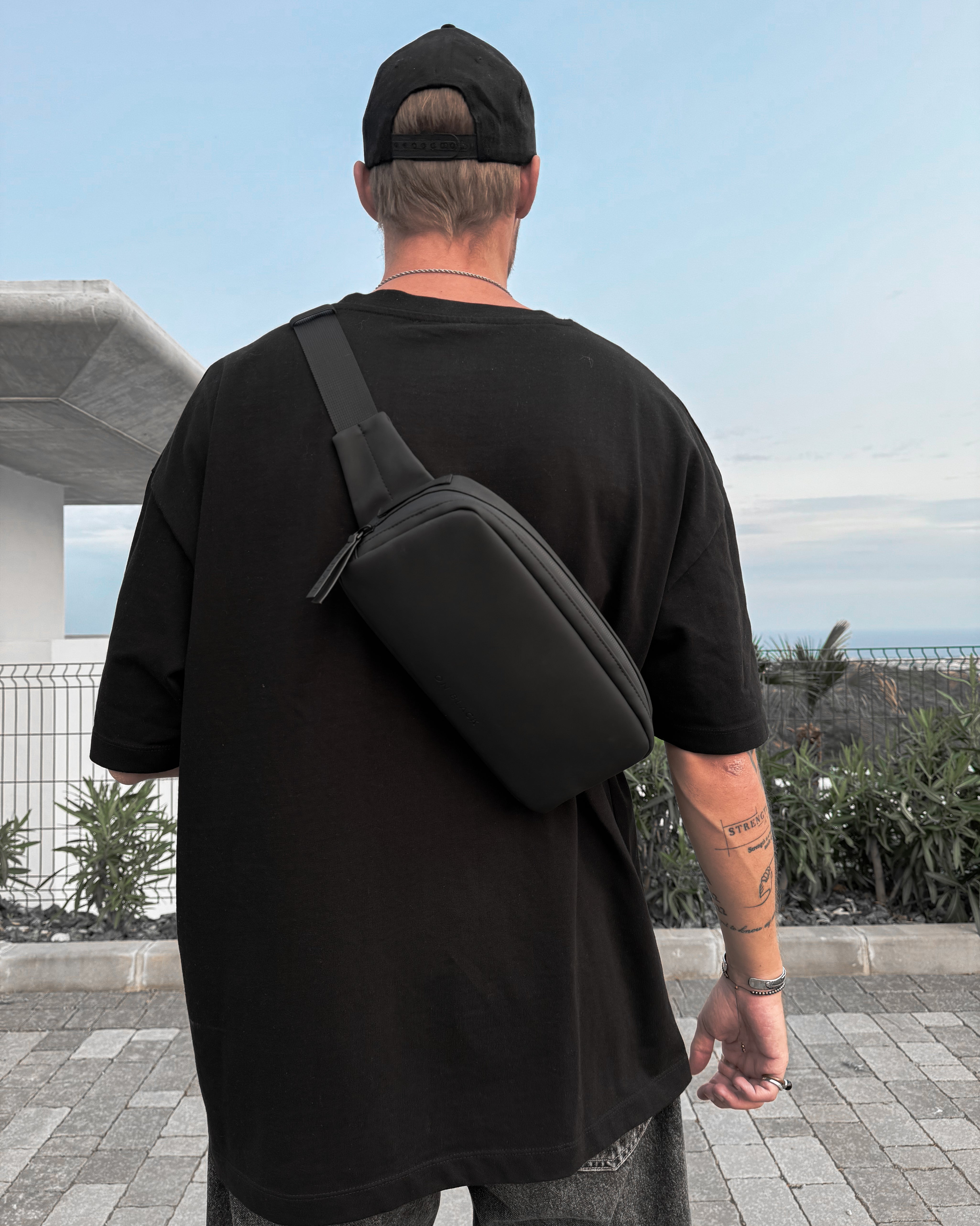 Person wearing a black t-shirt and carrying a black crossbody bag outdoors.